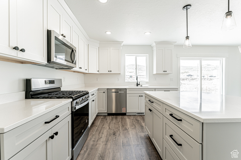 Kitchen with appliances with stainless steel finishes, a sink, dark wood-style flooring, recessed lighting, and decorative light fixtures