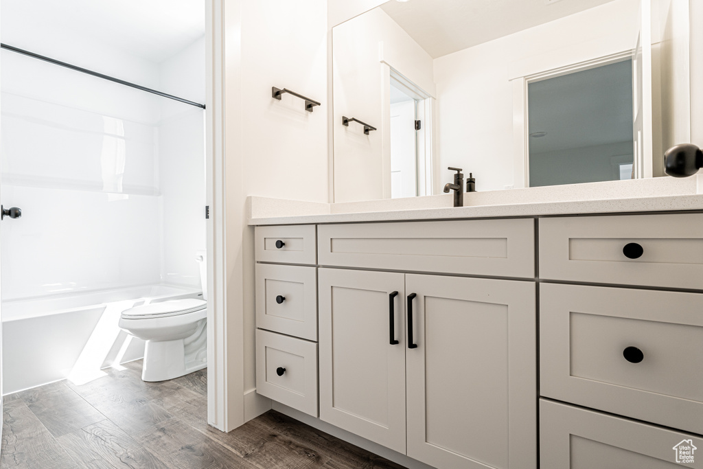 Bathroom with vanity, toilet, wood finished floors, and shower / washtub combination