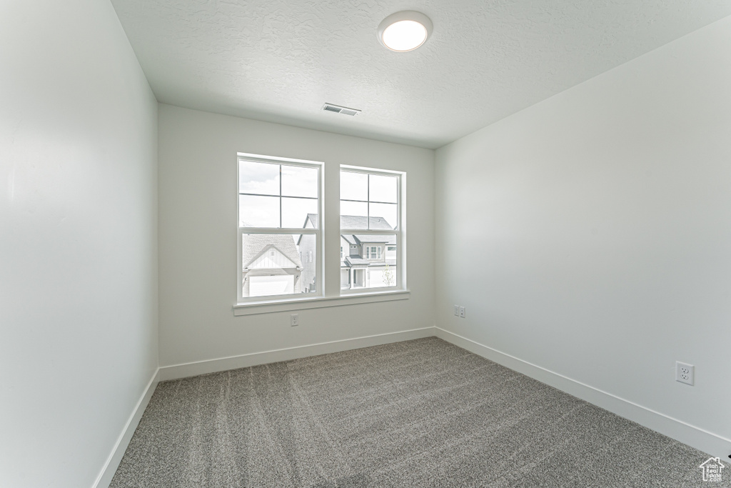 Empty room with a textured ceiling, baseboards, and carpet