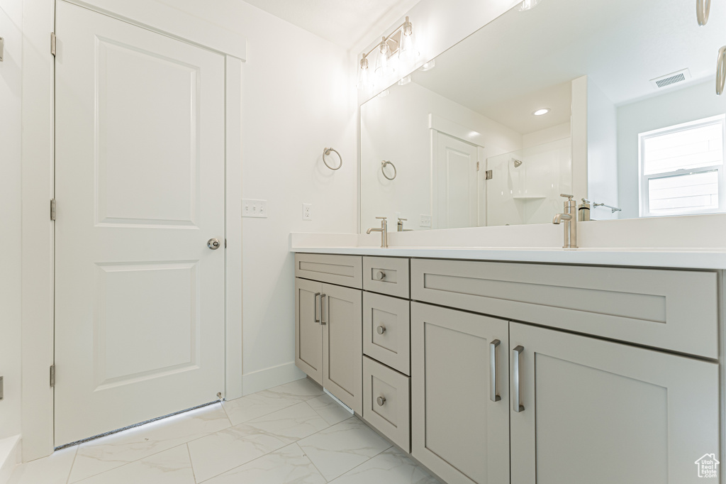 Full bathroom with double vanity, marble look tile flooring, baseboards, a shower, and recessed lighting
