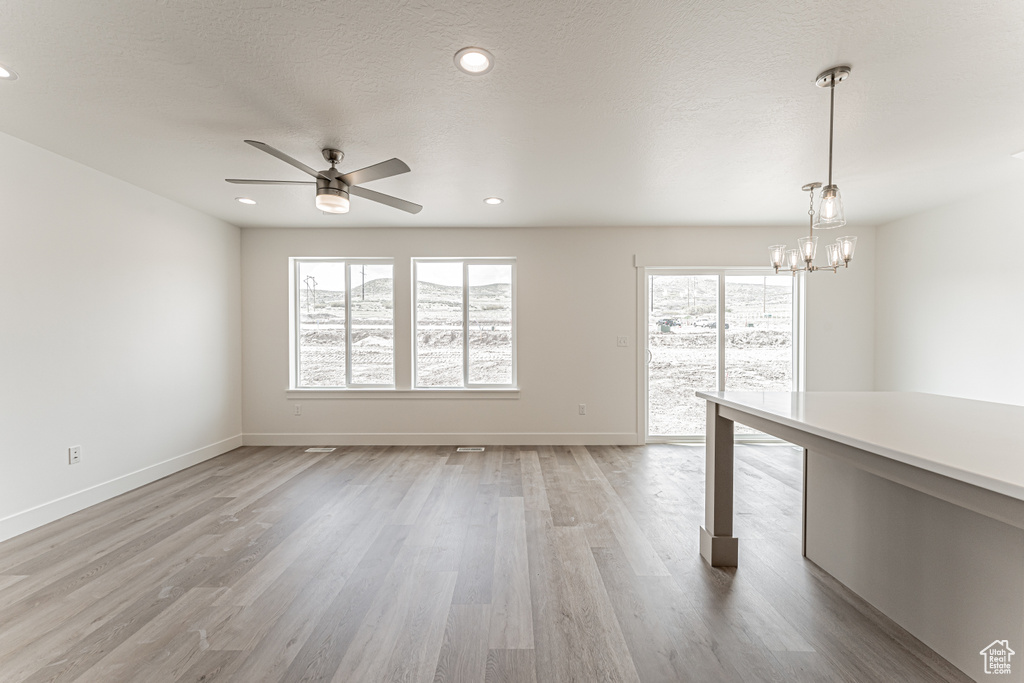 Empty room with a ceiling fan, healthy amount of natural light, light wood-style floors, a chandelier, and recessed lighting