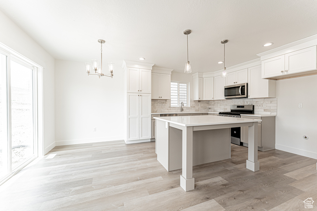 Kitchen featuring stainless steel appliances, decorative backsplash, light countertops, a center island, and recessed lighting