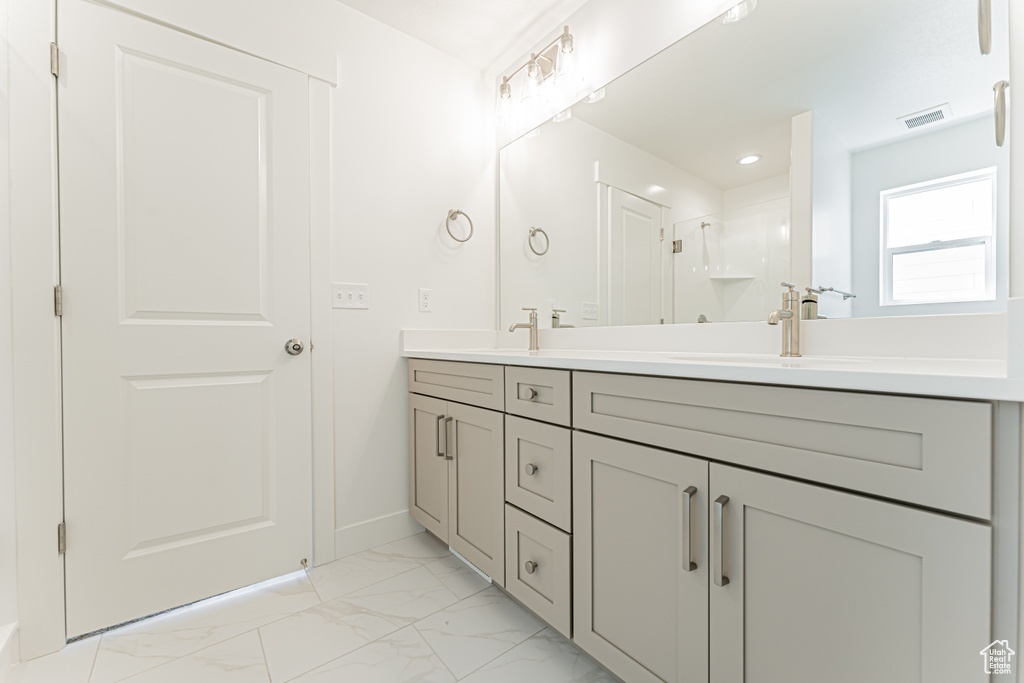 Full bath featuring double vanity, marble look tiles, a shower with door, baseboards, and recessed lighting