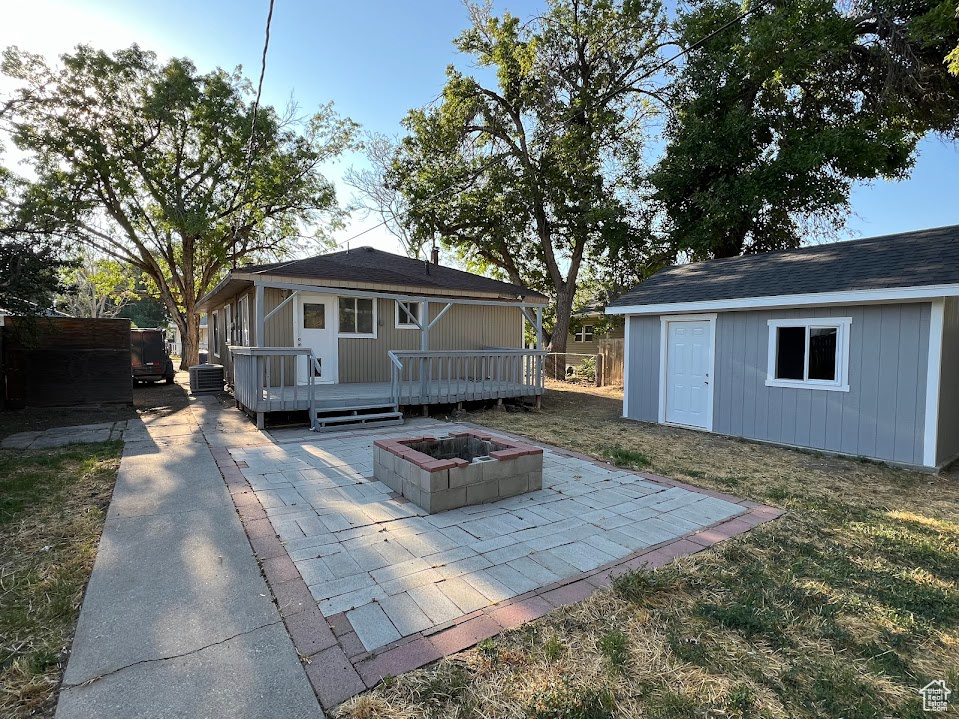 Back of property featuring an outbuilding, central AC unit, a patio, a fire pit, and a wooden deck