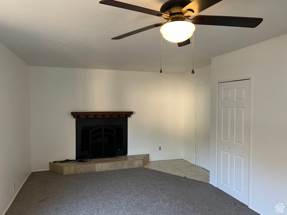 Unfurnished living room featuring a tiled fireplace, light colored carpet, and ceiling fan