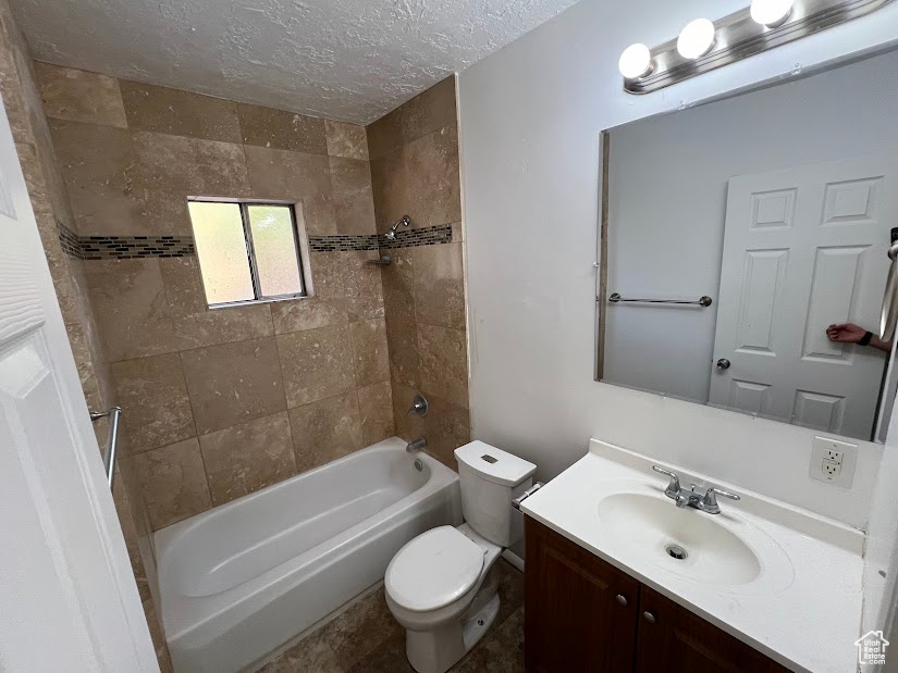 Full bathroom featuring tiled shower / bath combo, vanity, toilet, and a textured ceiling