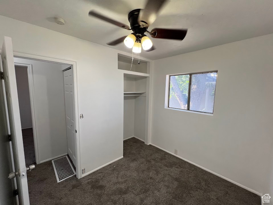 Unfurnished bedroom with a closet, ceiling fan, and dark colored carpet