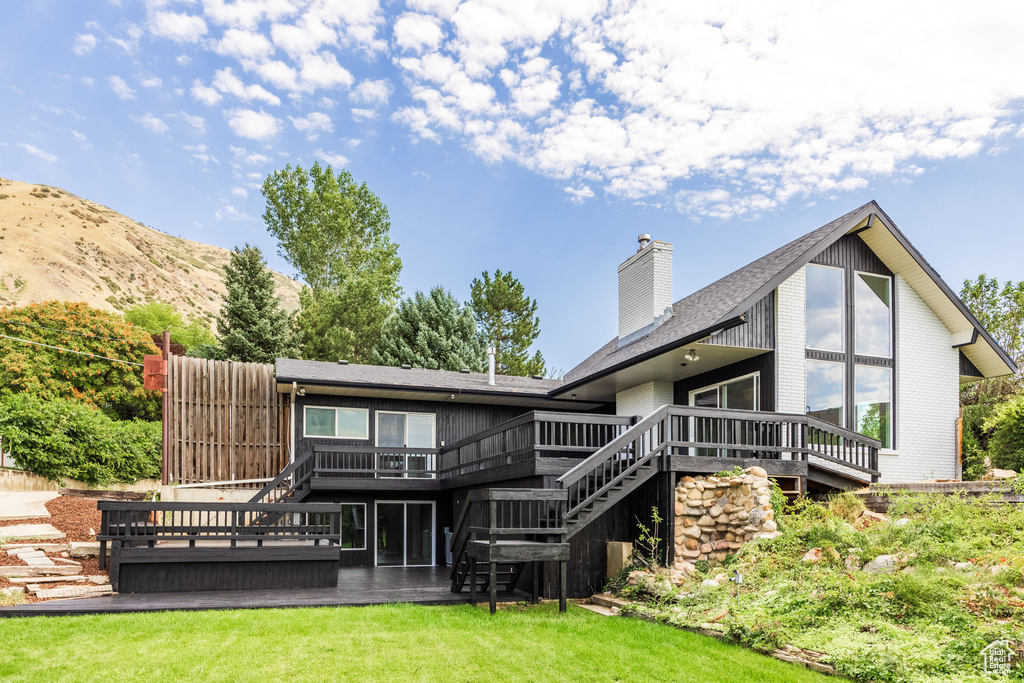 Back of property with a lawn and a deck with mountain view