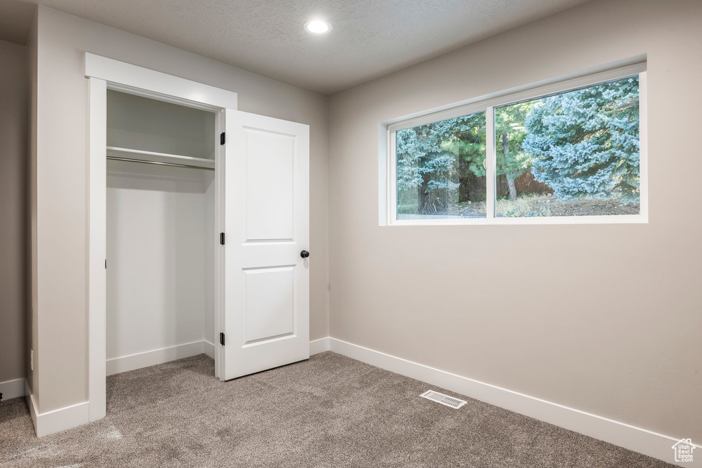 Unfurnished bedroom with light colored carpet, a textured ceiling, and a closet