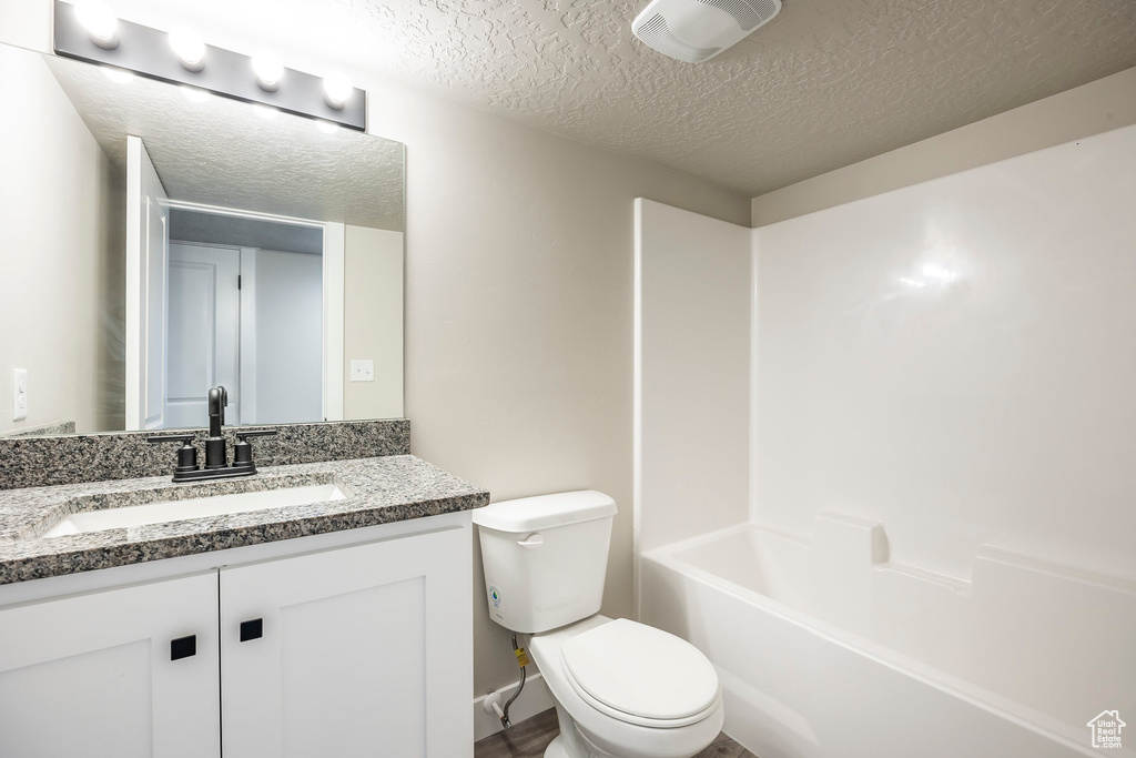 Full bathroom with vanity, a textured ceiling, toilet, and shower / bathing tub combination