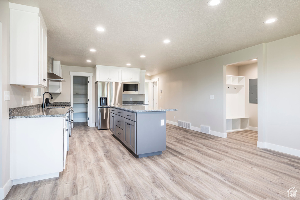 Kitchen featuring a kitchen island, light stone countertops, stainless steel appliances, and white cabinets