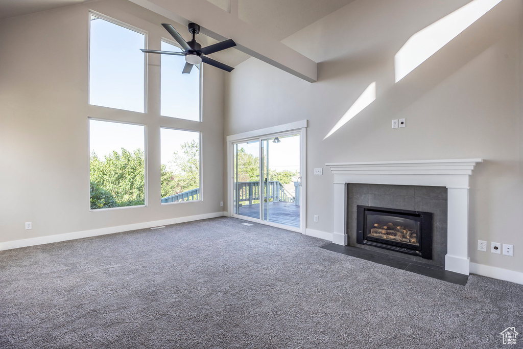 Unfurnished living room featuring dark carpet, a fireplace, beam ceiling, high vaulted ceiling, and ceiling fan