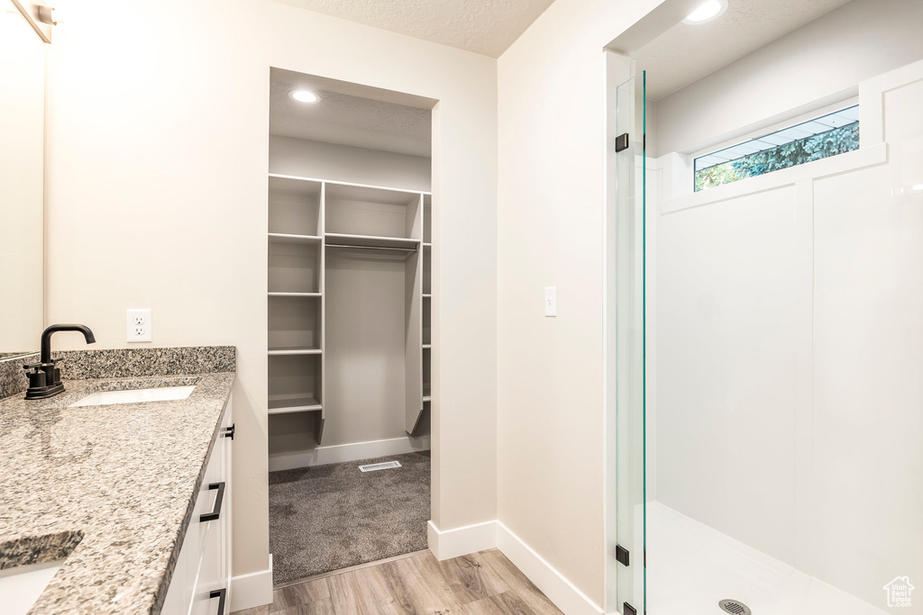 Bathroom with a textured ceiling, vanity, hardwood / wood-style flooring, and a shower with door