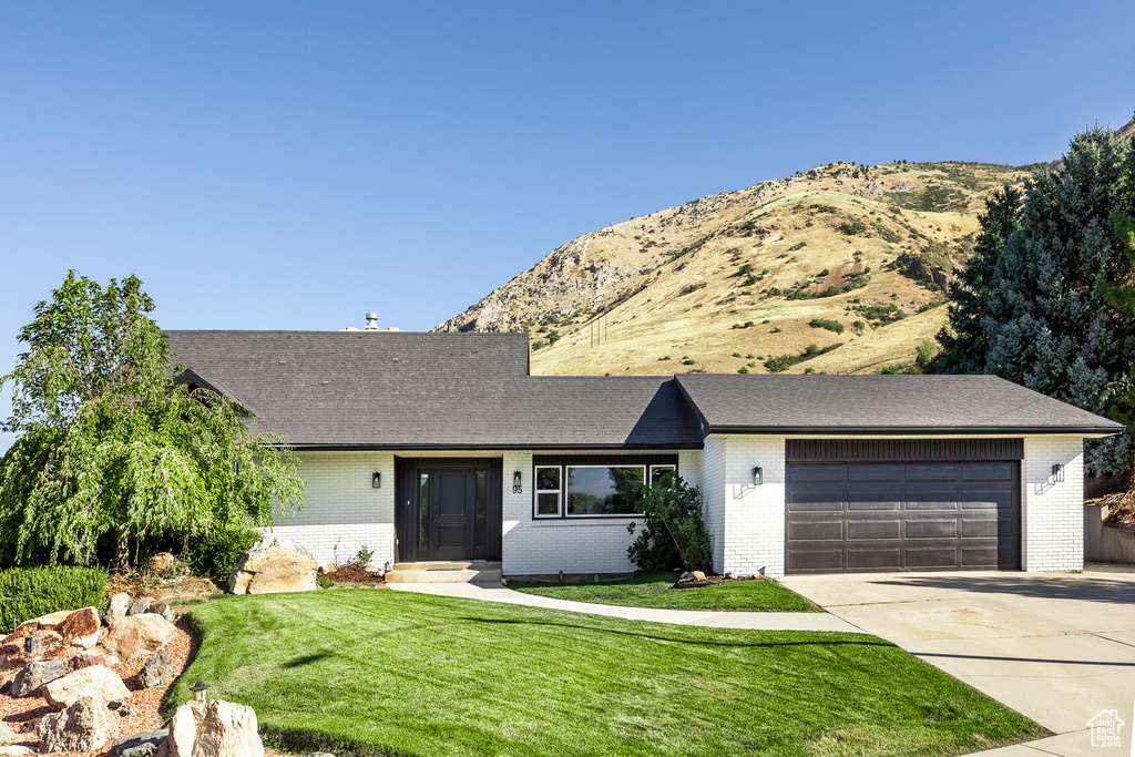 Ranch-style house with a front yard, a mountain view, and a garage