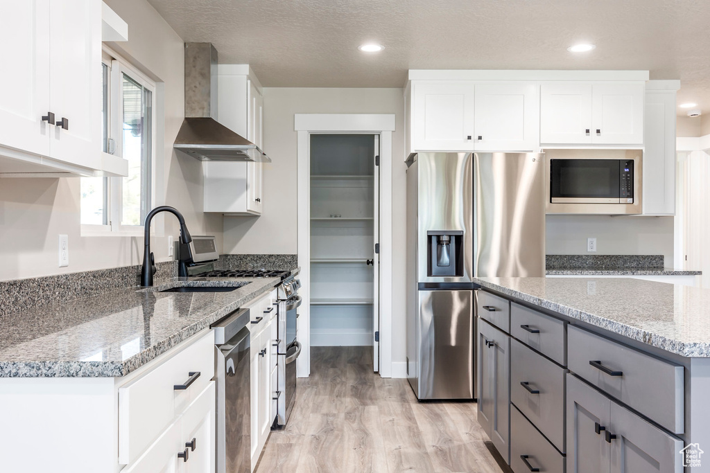 Kitchen with gray cabinetry, light stone counters, stainless steel appliances, wall chimney range hood, and white cabinets