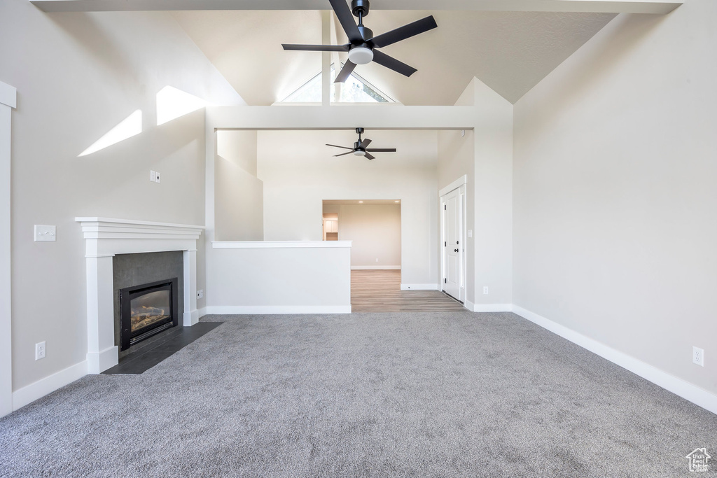 Unfurnished living room featuring high vaulted ceiling, a tiled fireplace, ceiling fan, and dark carpet