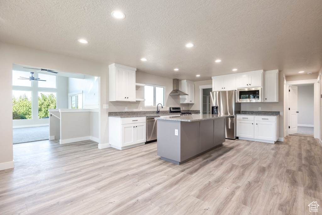 Kitchen with a kitchen island, white cabinetry, wall chimney exhaust hood, and stainless steel appliances