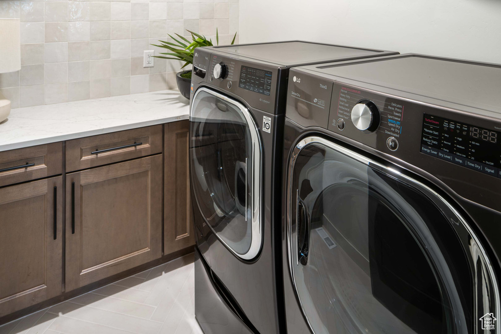 Washroom with light tile patterned floors, cabinets, and washer and clothes dryer