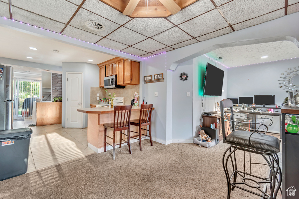 Kitchen featuring a breakfast bar area, light carpet, backsplash, kitchen peninsula, and white range with electric cooktop
