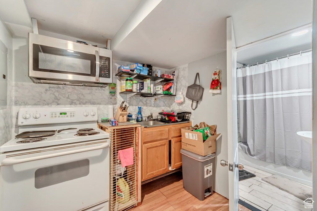 Kitchen with white electric stove, decorative backsplash, light hardwood / wood-style floors, and sink