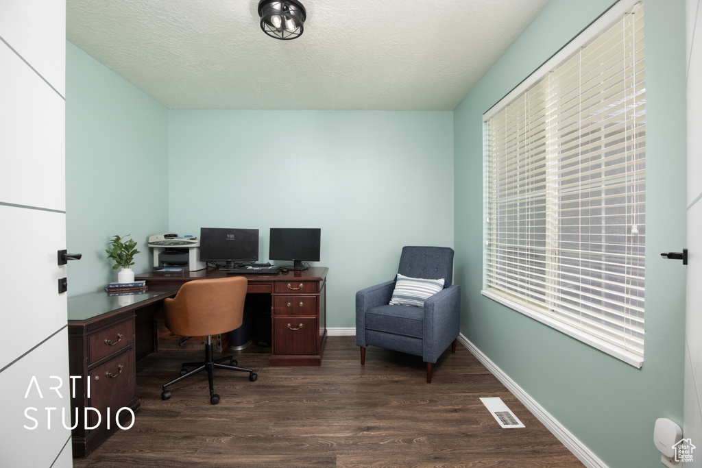 Home office with dark wood-type flooring, a textured ceiling, and a healthy amount of sunlight