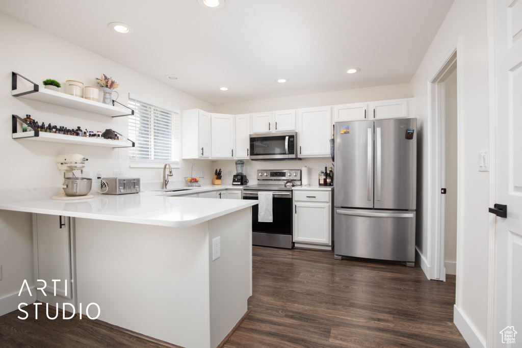 Kitchen featuring dark hardwood / wood-style flooring, kitchen peninsula, sink, appliances with stainless steel finishes, and white cabinets