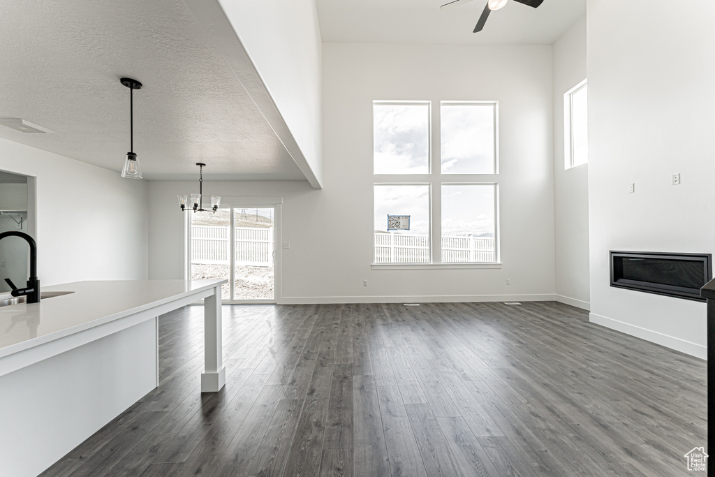 Unfurnished living room featuring ceiling fan, dark wood-style floors, a chandelier, a sink, and baseboards