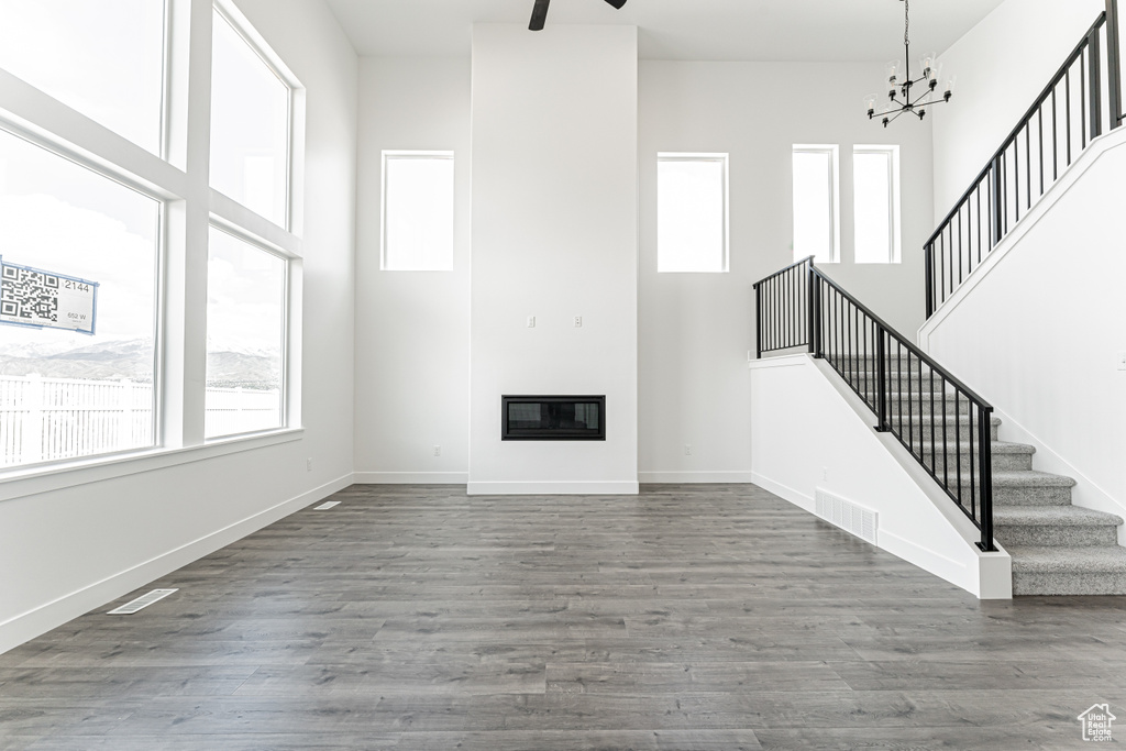 Unfurnished living room with stairs, a towering ceiling, wood finished floors, a chandelier, and baseboards