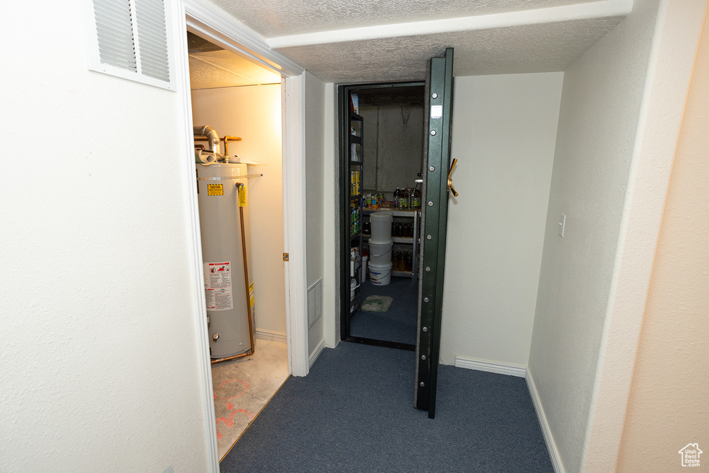 Corridor featuring a textured ceiling, carpet floors, and water heater