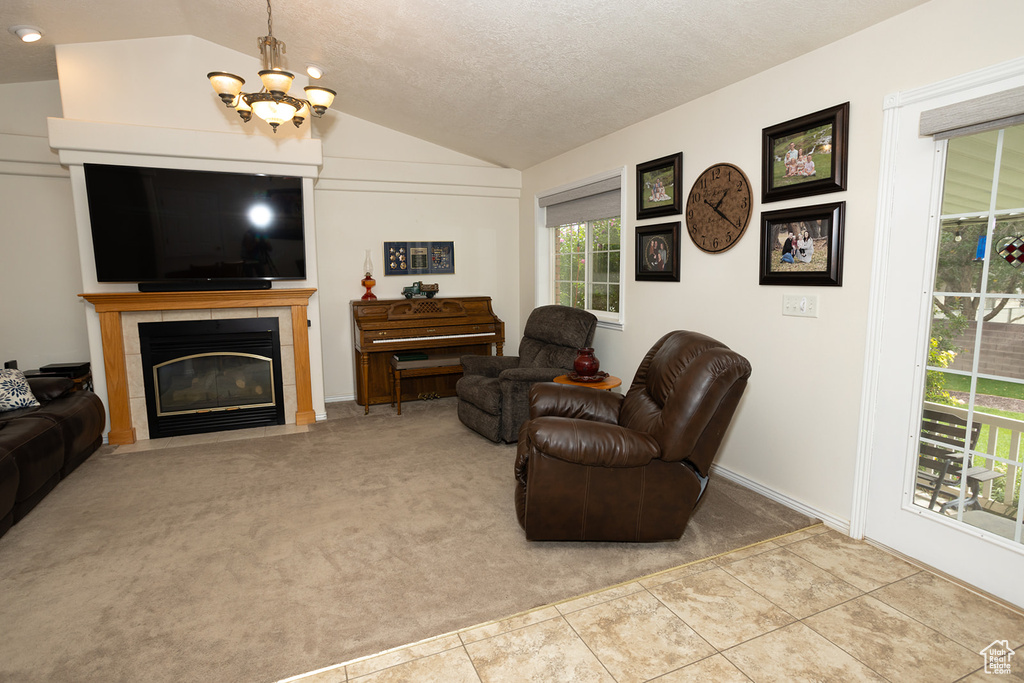 Carpeted living room featuring vaulted ceiling, a textured ceiling, an inviting chandelier, and a tile fireplace