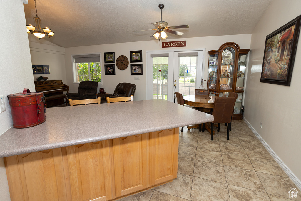 Kitchen featuring a textured ceiling, vaulted ceiling, light tile patterned floors, and ceiling fan with notable chandelier