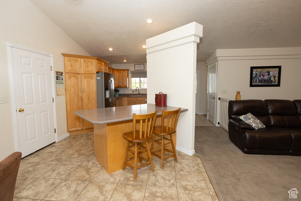 Kitchen featuring a breakfast bar area, stainless steel fridge with ice dispenser, kitchen peninsula, sink, and lofted ceiling