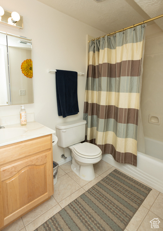 Full bathroom with tile patterned flooring, toilet, vanity, shower / bath combo with shower curtain, and a textured ceiling