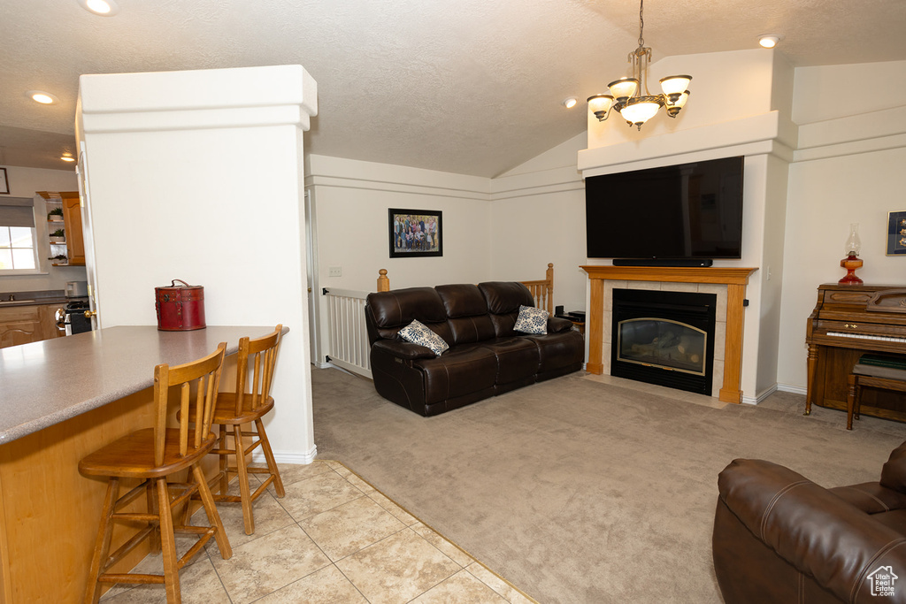 Carpeted living room featuring a tile fireplace, a chandelier, a textured ceiling, and vaulted ceiling