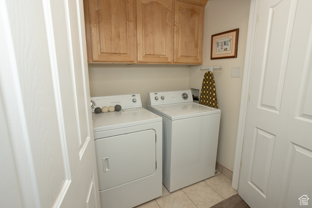 Laundry area with light tile patterned floors, washing machine and clothes dryer, and cabinets