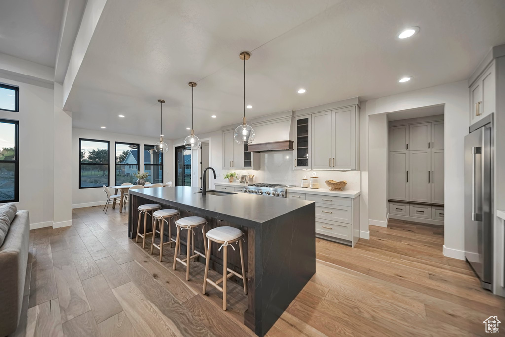 Kitchen featuring light wood-type flooring, pendant lighting, a large island with sink, sink, and premium range hood