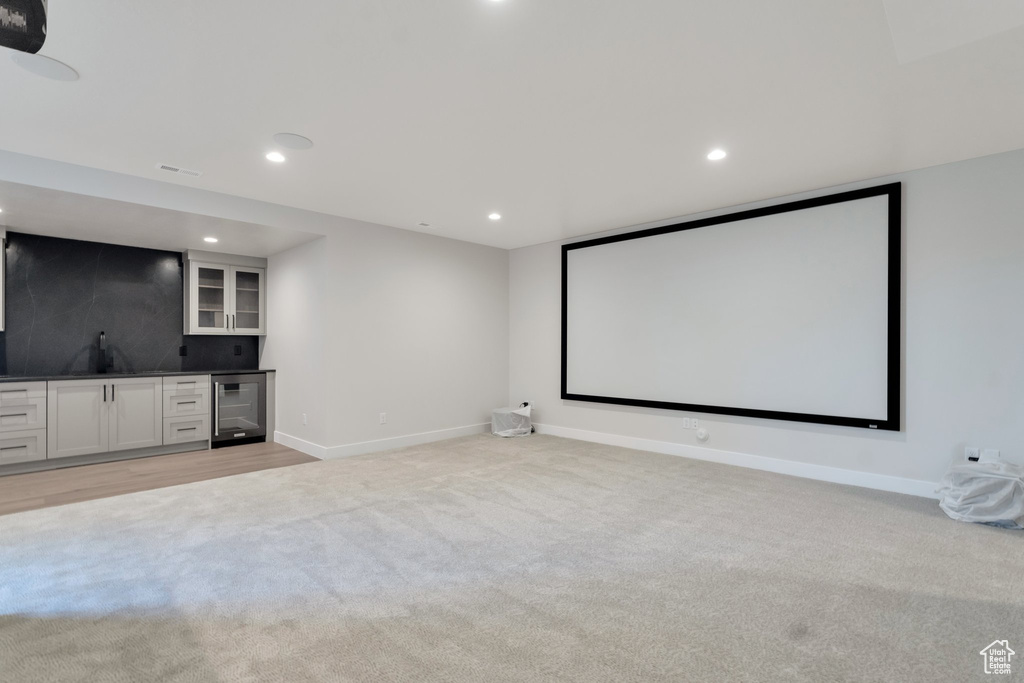 Home theater room with beverage cooler, light colored carpet, and indoor wet bar