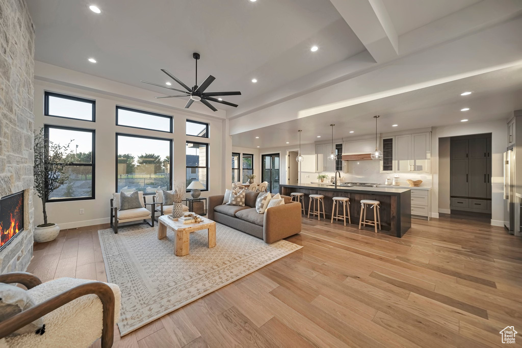 Living room with sink, ceiling fan, a stone fireplace, and light hardwood / wood-style flooring