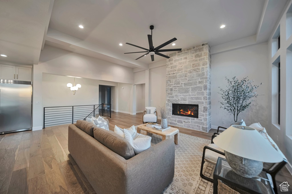 Living room with ceiling fan with notable chandelier, hardwood / wood-style flooring, and a fireplace