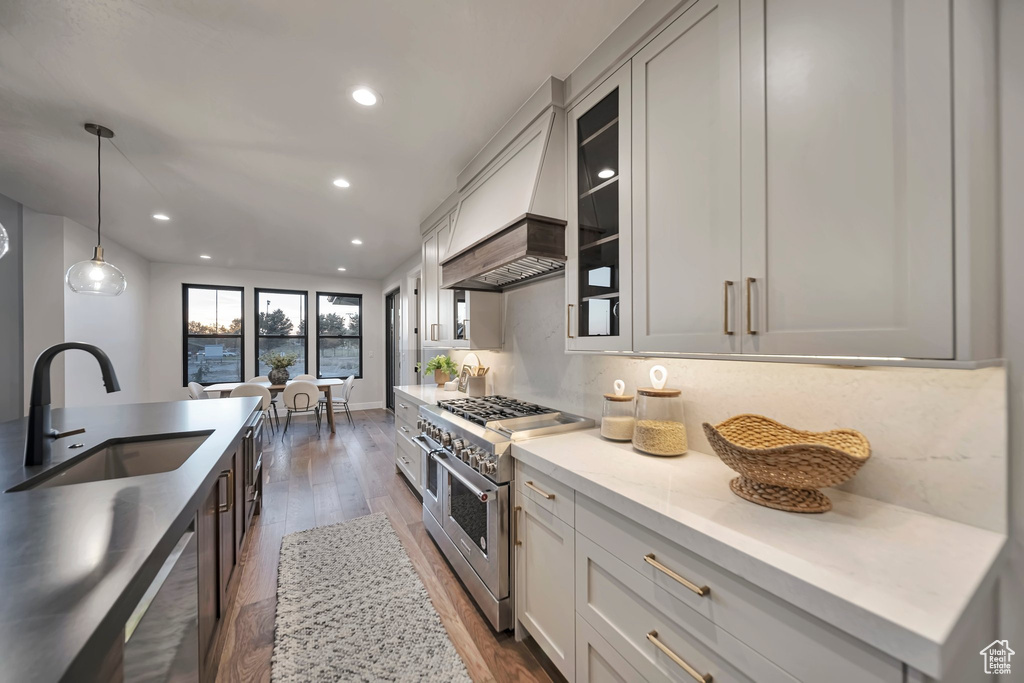 Kitchen with dark hardwood / wood-style flooring, custom range hood, light stone countertops, sink, and double oven range