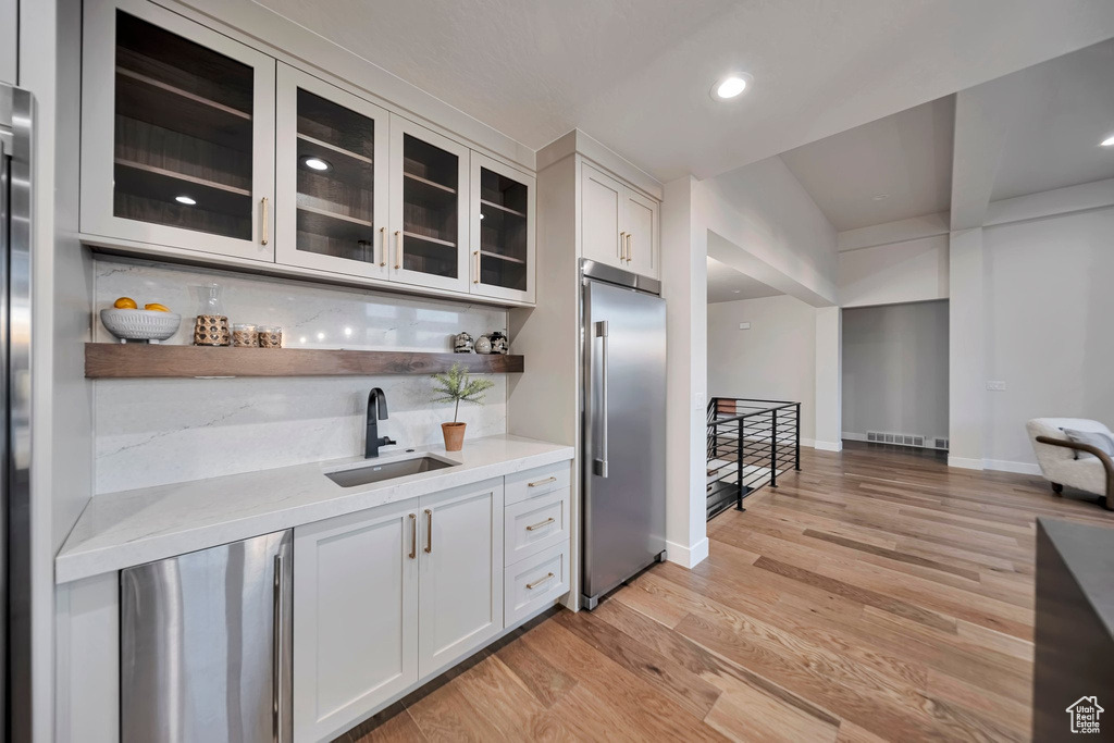 Kitchen featuring high end fridge, white cabinets, sink, and decorative backsplash