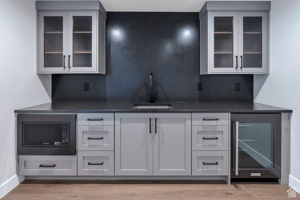 Bar with black microwave, sink, decorative backsplash, and beverage cooler