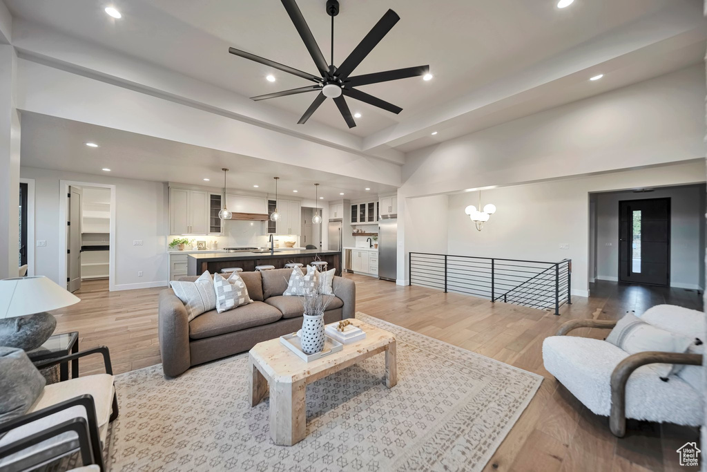 Living room featuring ceiling fan with notable chandelier, sink, and light hardwood / wood-style flooring