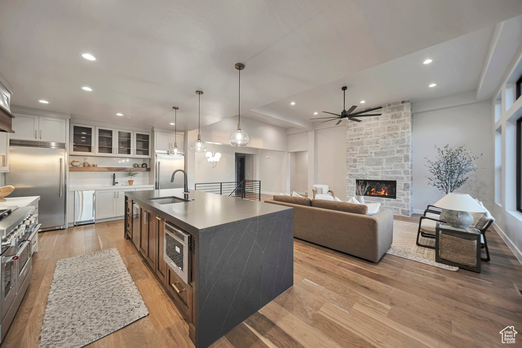 Kitchen with light hardwood / wood-style flooring, a kitchen island with sink, sink, and white cabinetry