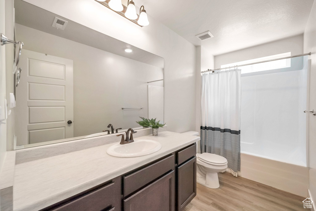 Full bathroom with vanity, toilet, hardwood / wood-style floors, and shower / bath combo with shower curtain