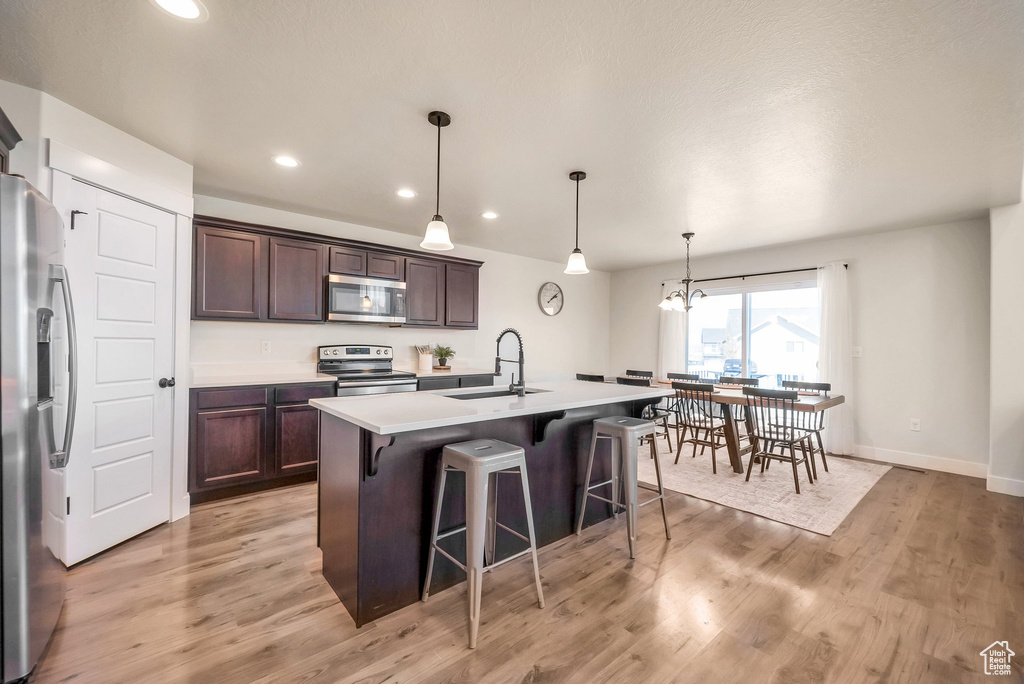 Kitchen with a kitchen island with sink, light wood-type flooring, stainless steel appliances, sink, and a breakfast bar