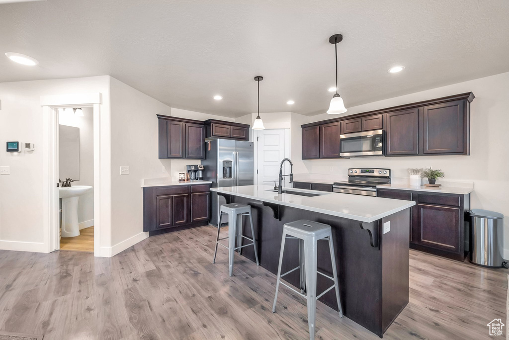 Kitchen featuring light hardwood / wood-style flooring, an island with sink, a kitchen bar, stainless steel appliances, and sink