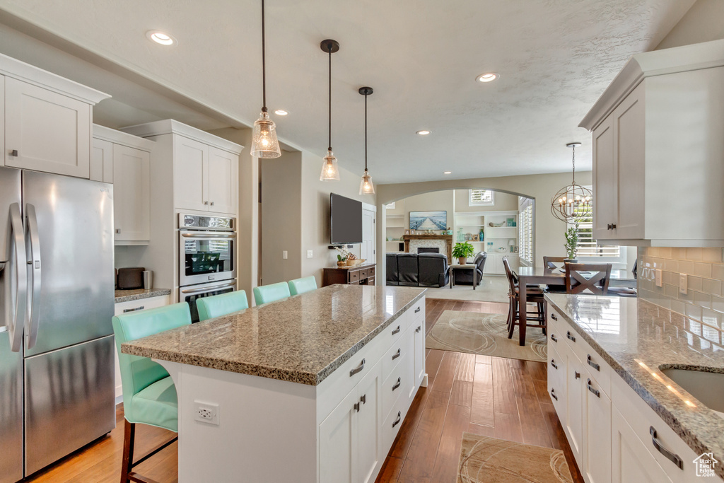 Kitchen with light wood-type flooring, stainless steel appliances, light stone countertops, and hanging light fixtures