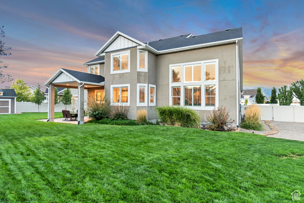 Back house at dusk featuring a yard and a patio