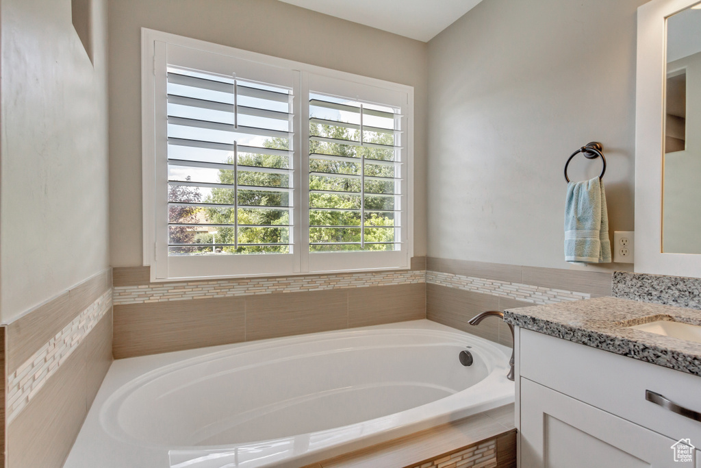 Bathroom with plenty of natural light, a relaxing tiled tub, and vanity